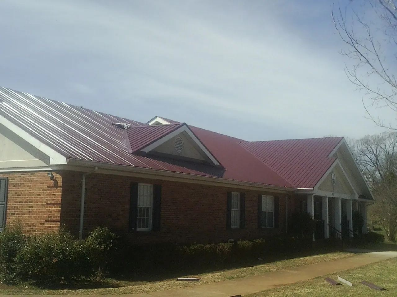 Red metal roof with gabled entries on a long brick building, from a Hail Damage Roof Repair job in Heppner