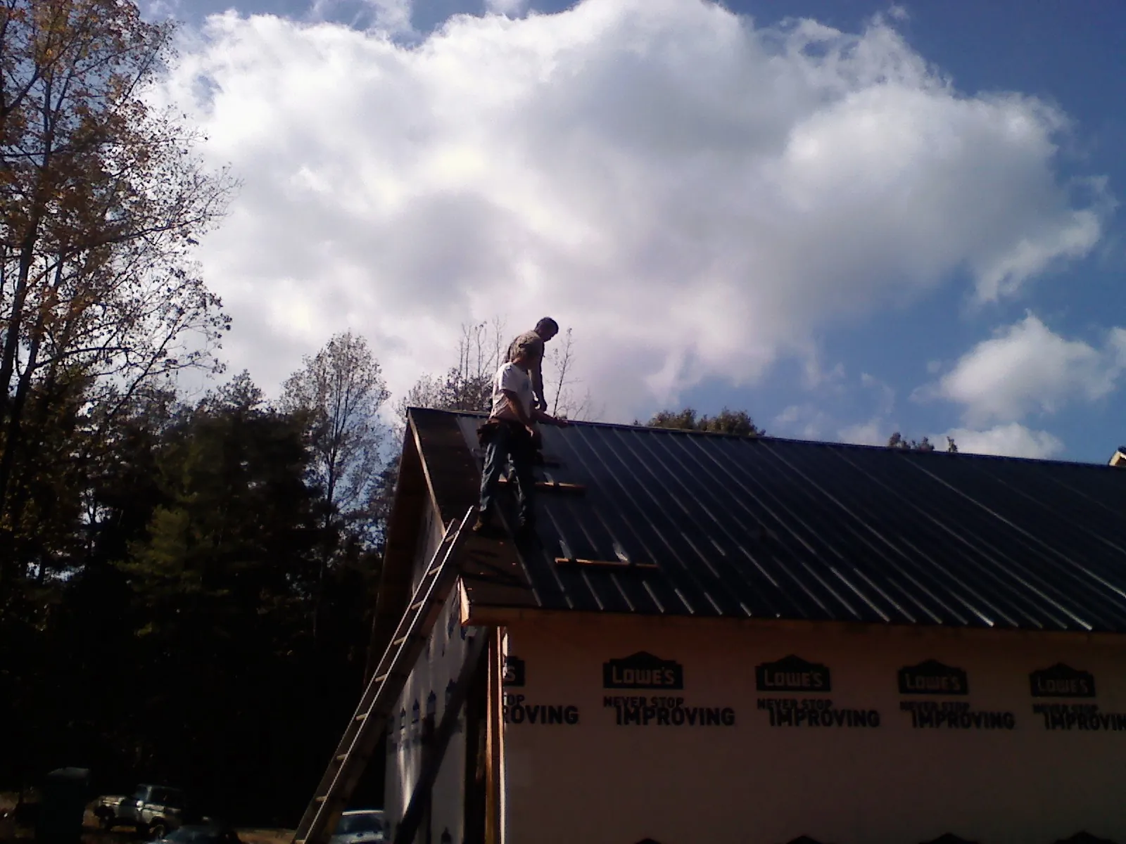Roofer fastening dark metal panels high against a cloudy sky, from a Roof Inspection job in Heppner
